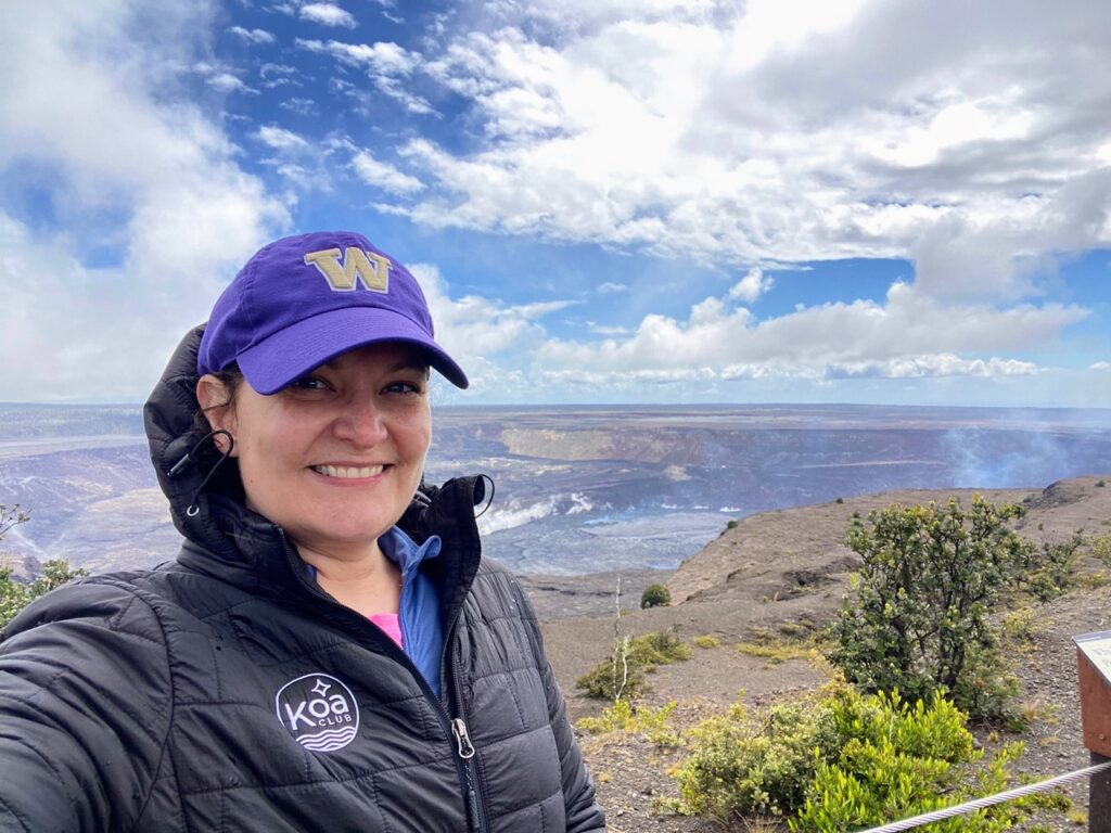 image shows a woman in a UW hat in front of the steam vents of Kilauea crater