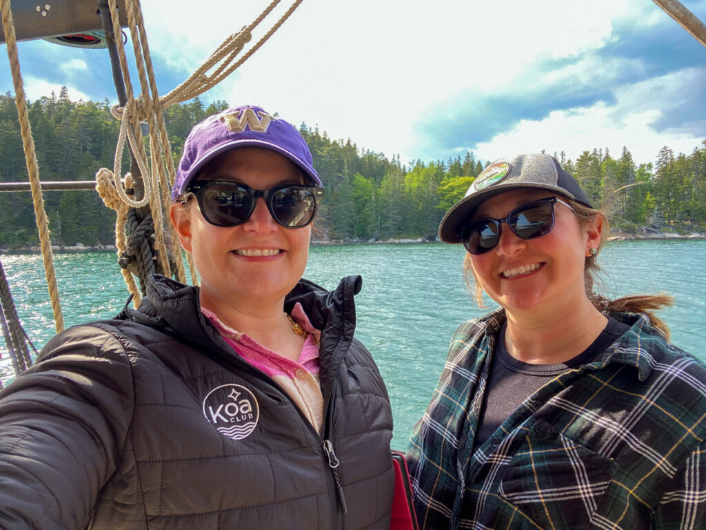 image shows two women standing on a boat with very blue water behind them