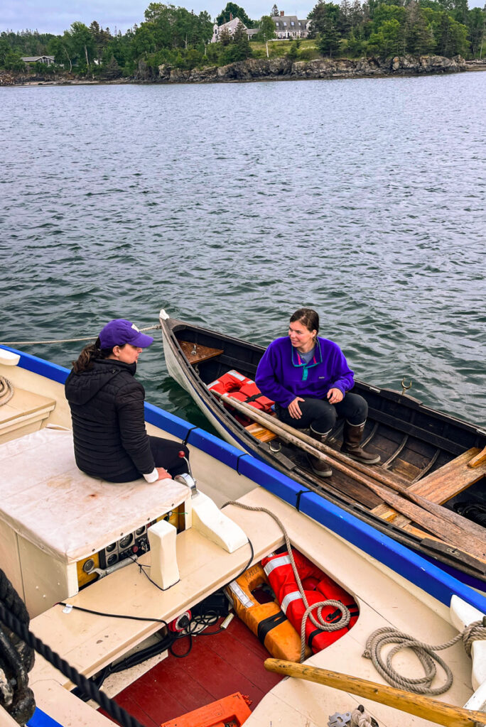 image shows two women, one in a rowboat and one in a yawl boat in a bay