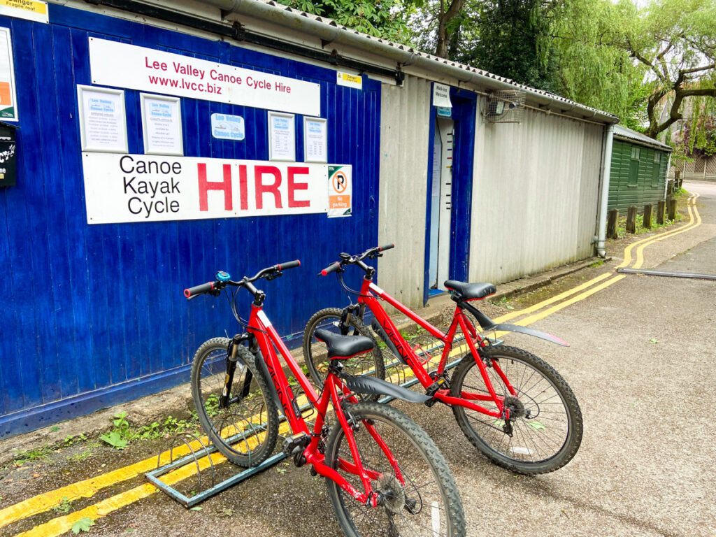 image shows two red bicycles outside a blue building that says HIRE on it