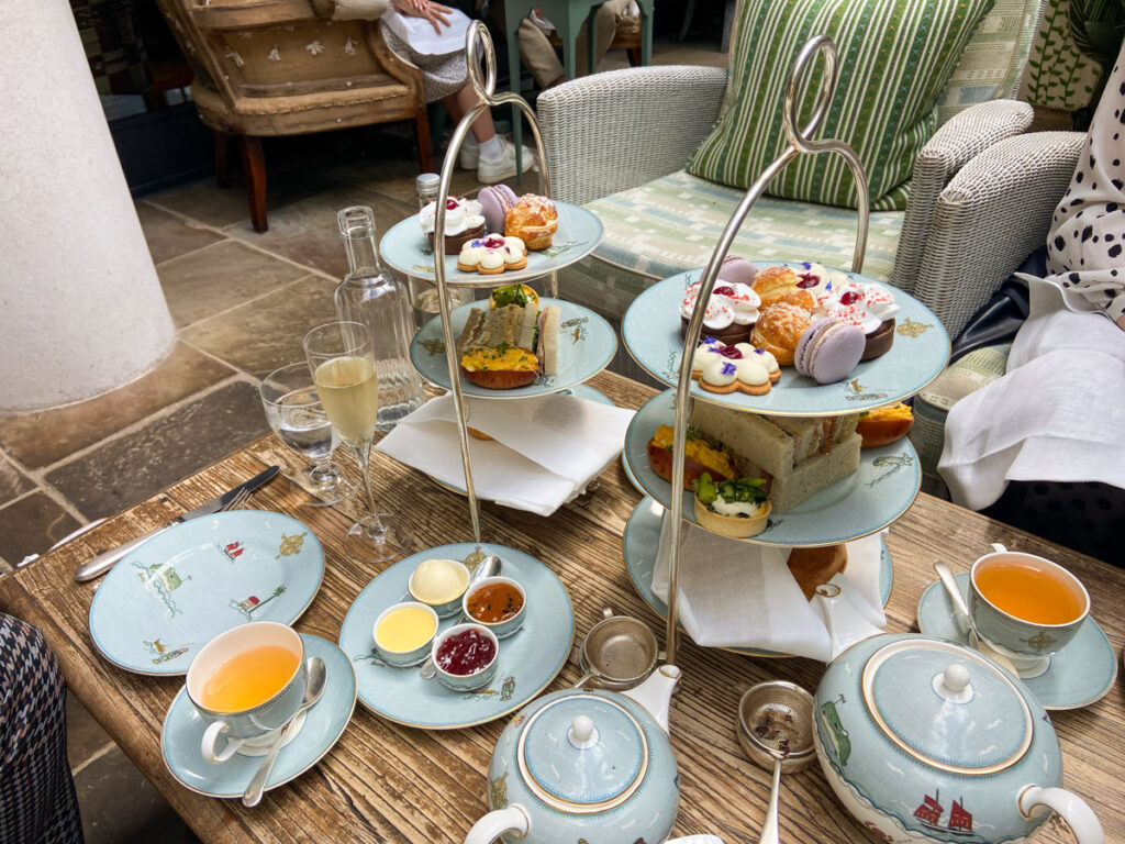 Image shows an afternoon tea spread at the Ham Yard hotel in London. Two three tiered stands hold an assortment of sweets and sandwiches, with tea and champagne.