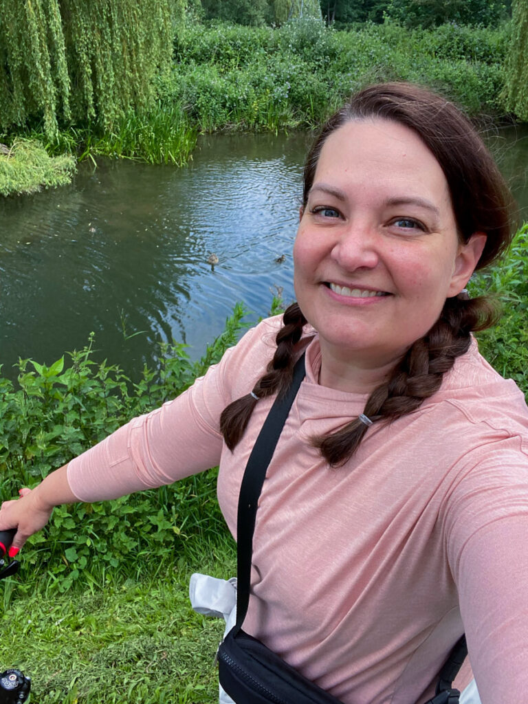 image shows a woman with pigtail braids and a pink shirt riding a bike by a canal