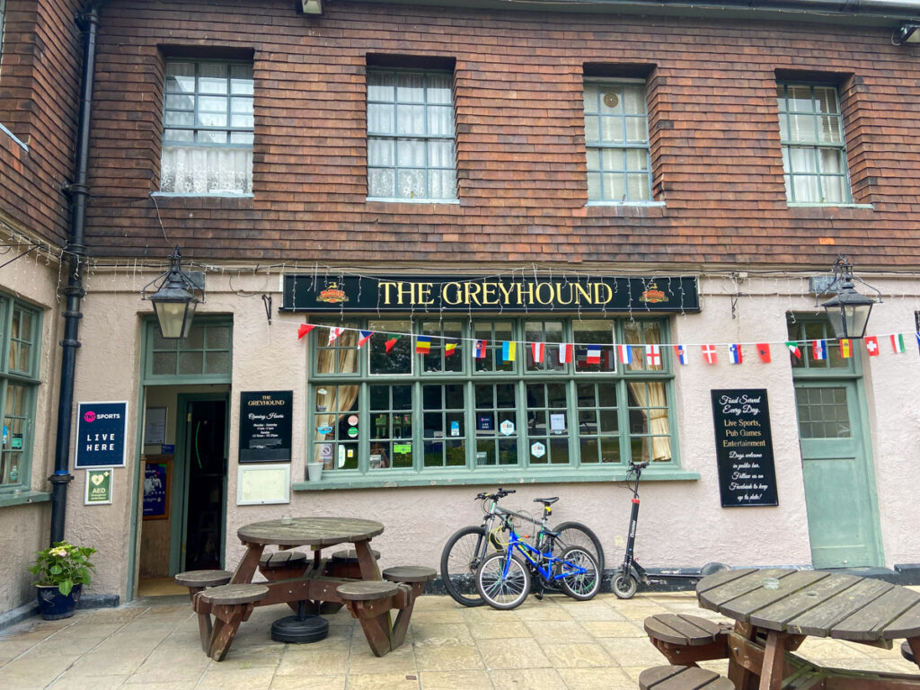 image shows a traditional english pub called The Greyhound with some bunting over a green paned window with a bicycle in front