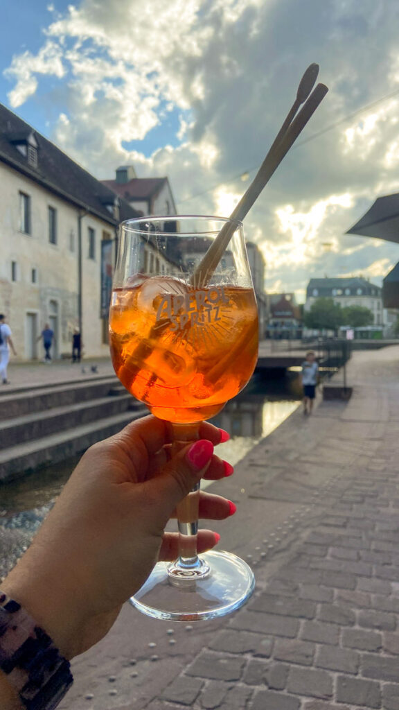 image shows an aperol spritz drink held up in front of a small town square