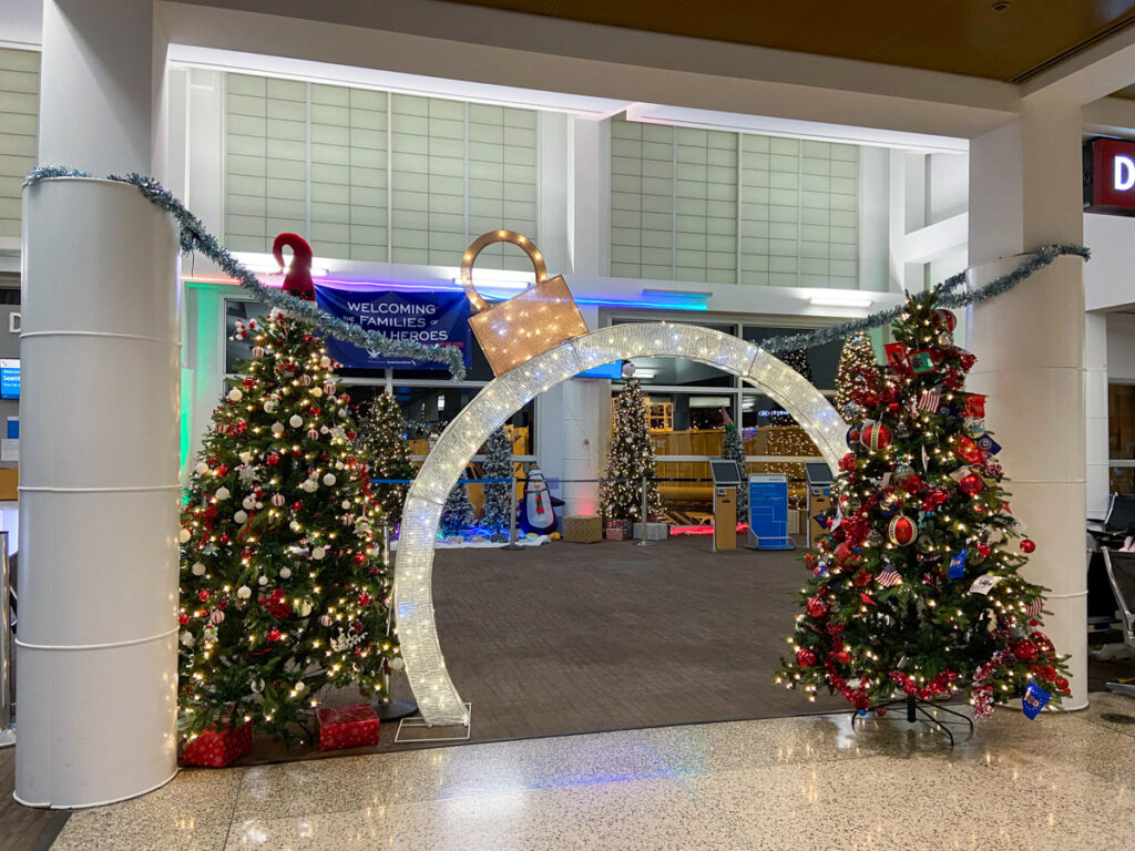 an airport is decorated for christmas with two decorated Christmas trees and an ornament cutout in front of a gate