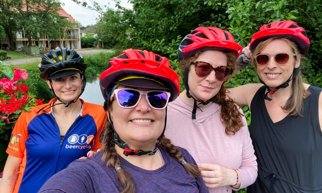 A group of cyclists wearing colorful rain gear, posing in front of a canal on a rainy day.