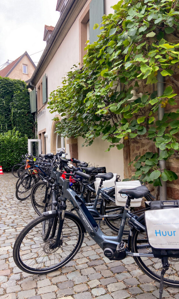 A dozen or so bicycles lined up on a cobblestone street in front of an old looking building.