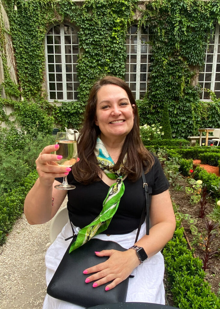 woman in a vintage scarf from ebay holds up a glass of white wine in a garden